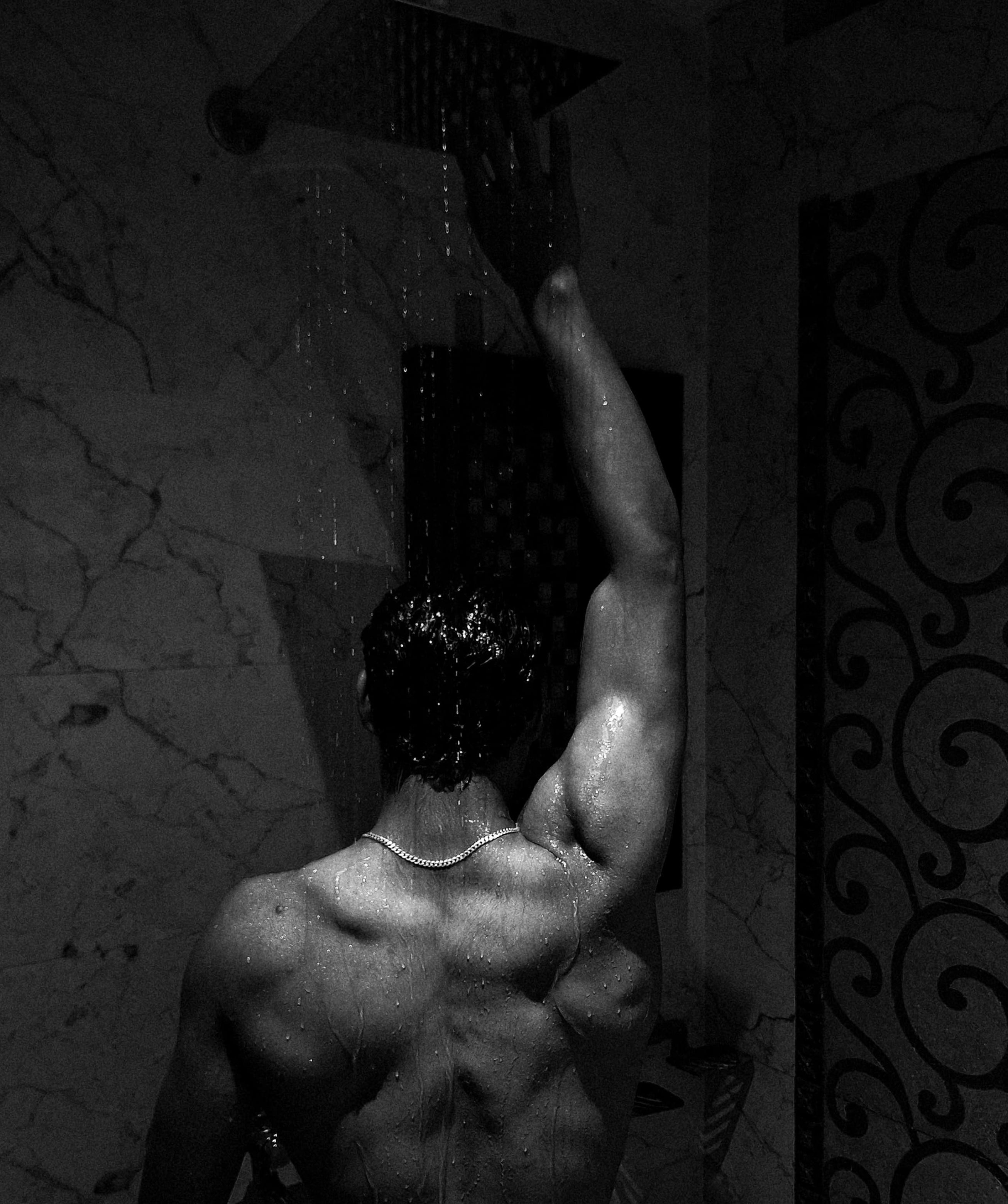 Person showering in a dimly lit bathroom with decorative tiles.